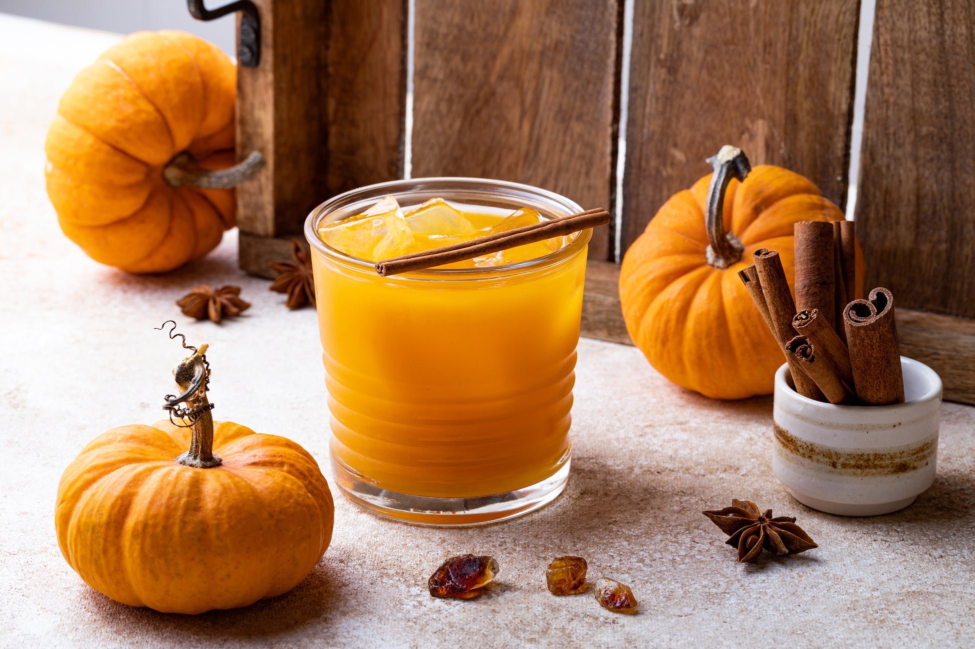 A glass of burbon with small pumkins around and a glass of cinnamon sticks